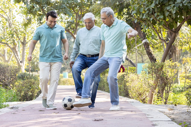 Two senior men and one young man were having fun with a football in a garden footpath.